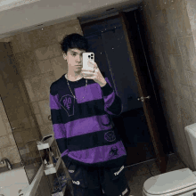 a young man is taking a selfie in a bathroom while wearing a purple and black striped sweater .