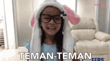 a little girl wearing glasses and a bunny hat says " teman-teman "