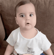 a baby wearing a white shirt that says sweet dreams is sitting on a couch