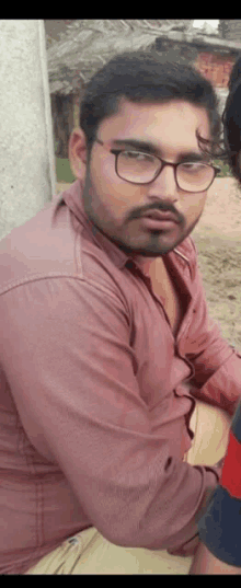 a man wearing glasses and a pink shirt is sitting on a wooden bench .