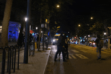 a group of people walking down a street at night with a van in the background that says ii