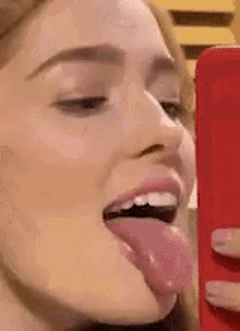 a woman is sticking her tongue out while taking a selfie with a cell phone .