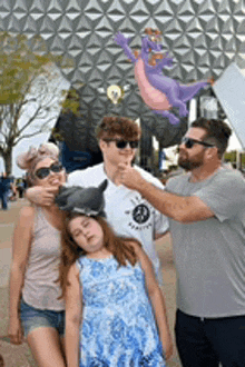 a family is posing for a picture in front of a building with a dragon flying in the background .