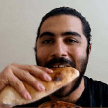 a man with a beard is biting into a piece of bread