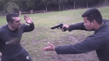 a man is pointing a gun at another man while they are fighting in a field .