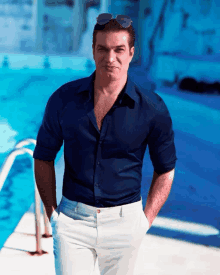 a man in a blue shirt and white pants stands in front of a blue pool