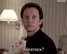 a man in a black shirt is holding a box of kleenex .