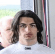 a young man with long dark hair is wearing a white shirt .