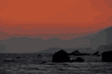 a sunset over the ocean with mountains in the background