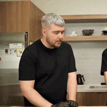 a man in a black shirt stands in a kitchen with a sticker on the refrigerator that says ' a ' on it