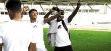 a group of young men are standing on a soccer field taking a picture of themselves with their phones .