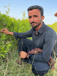 a man in a black shirt is kneeling in the grass looking at a plant