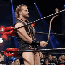 a man in a wrestling ring holds a rope in front of a crowd wearing a shirt that says bullet club