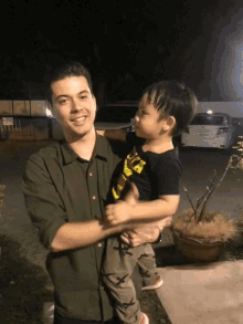 a man in a green shirt holds a little boy in a black shirt that says ' a ' on it