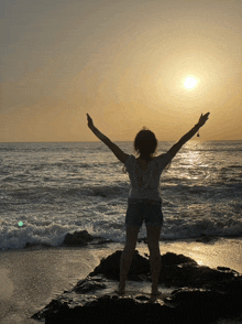 a woman stands on a beach with her arms outstretched