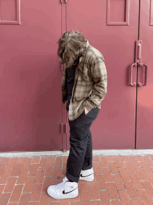 a man wearing a plaid shirt and black pants is standing in front of a red door