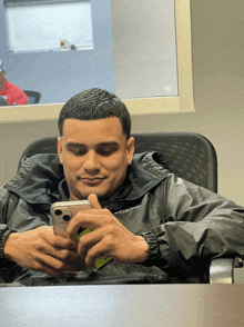 a man in a columbia jacket sits at a table looking at his phone