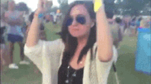 a woman wearing sunglasses and a white cardigan is standing in front of a crowd at a music festival .