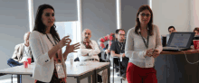 two women are standing in front of a group of people and one has a name tag that says ' a. ' on it