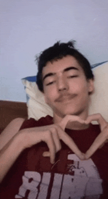 a young man is making a heart shape with his hands while laying in bed .