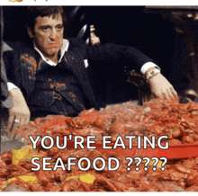 a man in a suit is sitting in front of a pile of seafood with the caption you 're eating seafood