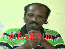 a man in a green and black striped shirt is holding a microphone and the word kottai is written in red on his shirt