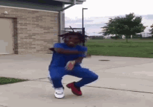 a young man in a blue shirt and blue pants is dancing on a sidewalk in front of a brick building .