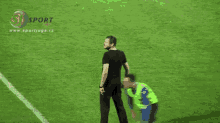 a man in a black shirt stands on a soccer field in front of a sign that says sport liga