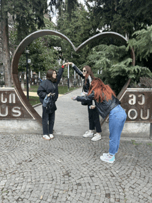 three girls are posing for a picture in front of a heart shaped sculpture that says un us ou