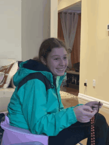 a girl in a green jacket sits on a pink stool