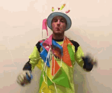 a man in a clown costume is holding balloons and wearing a hat and gloves .