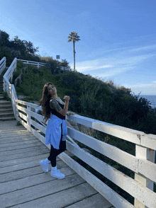 a woman stands on a wooden bridge overlooking the ocean