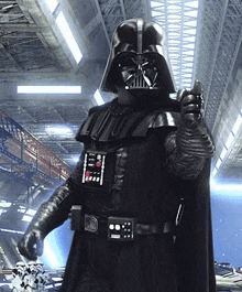 darth vader is giving a thumbs up in a warehouse while wearing a black costume .