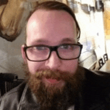 a man with a beard and glasses is standing in front of a deer head .