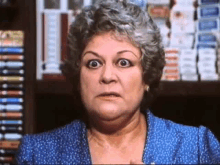 a woman in a blue dress is making a funny face in front of a shelf of books .