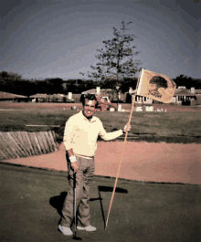 a man in a yellow shirt holds a golf club and a flag with a tree on it that says ' oak tree '