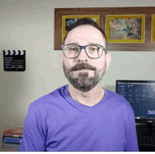 a man wearing glasses and a purple shirt stands in front of a computer