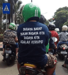 a man wearing a shirt that says budaya barat bukan budaya kita budaya kita adalah korupsi is riding a motorcycle