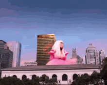 a woman in a pink dress is sitting on top of a building with a city skyline in the background