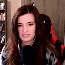 a woman wearing headphones and a red chair is talking into a microphone while sitting in front of a bookshelf .