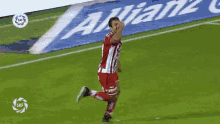 a man in a red and white uniform is running on a soccer field in front of an allianz banner