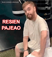 a man with a beard is sitting in front of a sign that says resien pajao