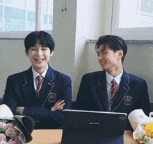 two boys in school uniforms are sitting at a table with a laptop that says enhypen on it