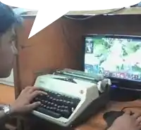 a man is typing on a typewriter next to a computer monitor