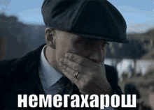 a man wearing a hat covering his mouth with his hand with the word nemegaxapoh written on the bottom