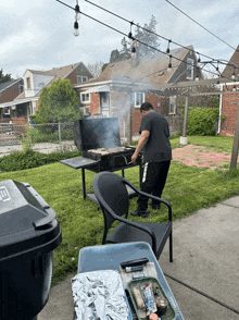 a man cooking on a grill in a backyard with a trash can that says ' a ' on it