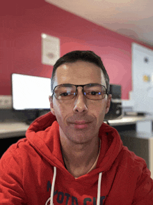 a man wearing glasses and a red hoodie with the word moto on the front