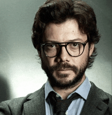 a man with a beard wearing glasses and a suit and tie is looking at the camera .