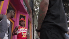 a man wearing a hawks jersey is standing in front of a pink door