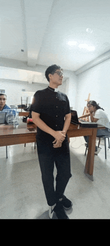 a man wearing a clergy collar stands in front of a wooden table